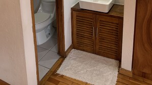 A small bathroom with a toilet, sink, mirror, and wooden cabinets. - Suite Centro Histórico (Quito)