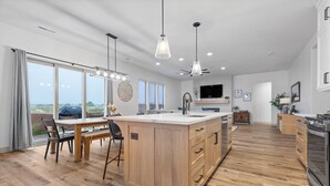 Een moderne keuken met een centraal eiland, houten vloer, hanglampen en een groot raam met uitzicht op de omgeving.