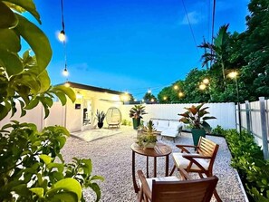 Relax in a serene patio setting with a small table and two chairs, surrounded by lush greenery and string lights.