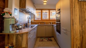 Een compacte keuken met houten details, een inbouwoven en een raam met houten jaloezieën.