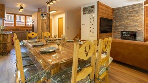 Een eetgedeelte met een lange houten tafel, transparante glazen stoelen en een open haard.