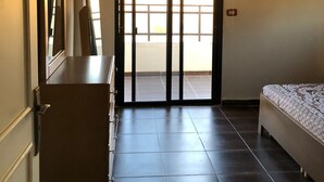 Ein Hotelzimmer mit Bett, Kommode, Spiegel und einer Schiebetür, die auf einen Balkon führt.