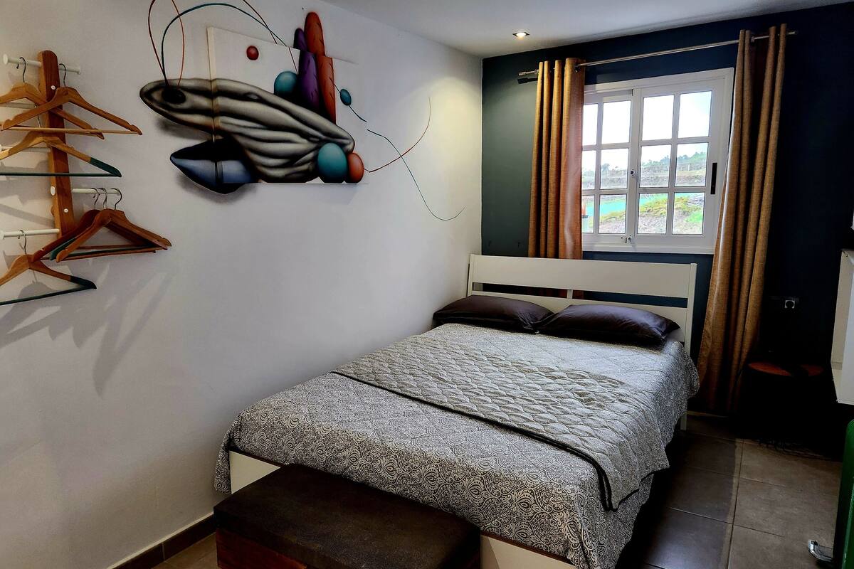Un dormitorio con cama, un banco, perchero en la pared y una ventana con cortinas.