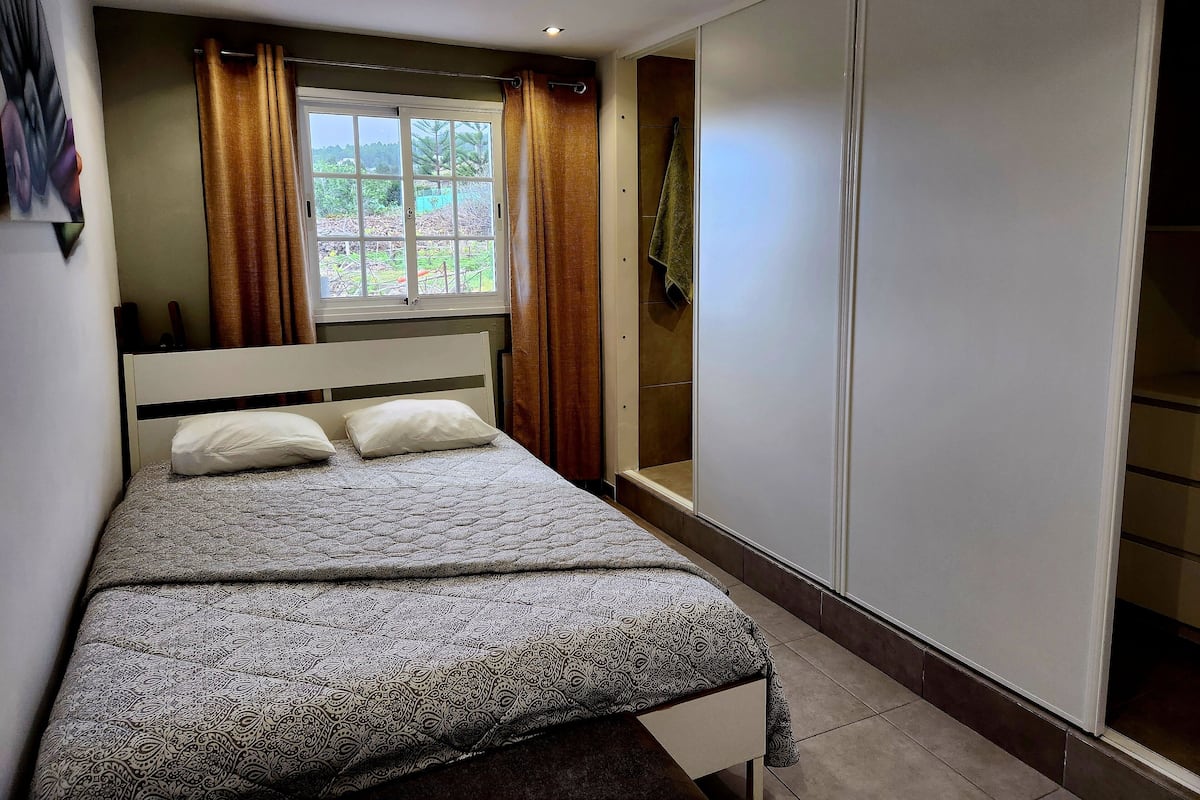 Un dormitorio con cama, ventana con cortinas, armario y vistas al exterior.