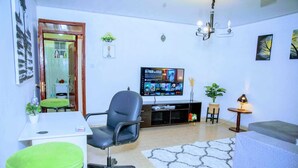A living room with a TV, a desk, a chair, and a sofa.
