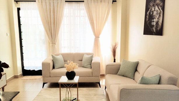 A living room with a beige sofa, a white coffee table, and a large window with sheer curtains.
