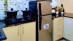 A kitchen with a stove, two pots, a refrigerator, and a microwave.