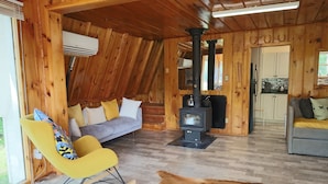 Ein Holzblockhaus-Interieur mit einer Couch, einem Schaukelstuhl, einem Herd und einem Kuhfellteppich.