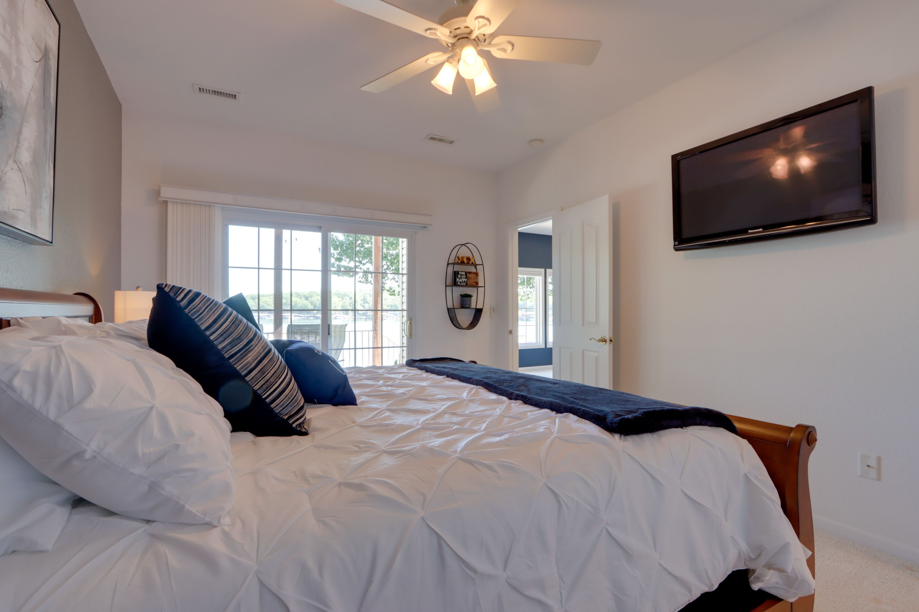 A bedroom with a bed, a ceiling fan, a TV, and a window with curtains.