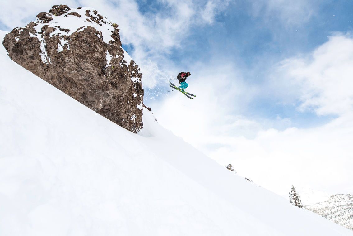 A skier mid-air performing a jump over a snow-covered slope.