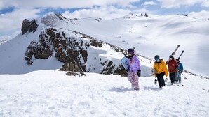 Un groupe de personnes fait de la randonnée dans une montagne enneigée, parsemée d’affleurements rocheux, sous un ciel dégagé.