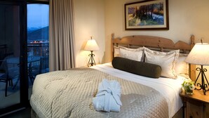 A hotel room with a large bed, two bedside lamps, a painting on the wall, and a balcony with chairs. - Beautiful Spacious King Room | Heated Pool (Park City)