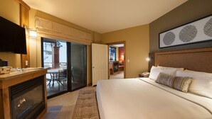 A hotel room with a bed, a TV, a fireplace, a balcony with a table and chairs, and a hallway leading to another room. - Deluxe Room + Ski-in/Ski-out Access to Slopes! (Park City)