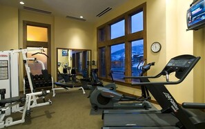 Ein Fitnessstudio mit Cardiogeräten, Gewichten und großen Fenstern mit Blick auf eine verschneite Landschaft.