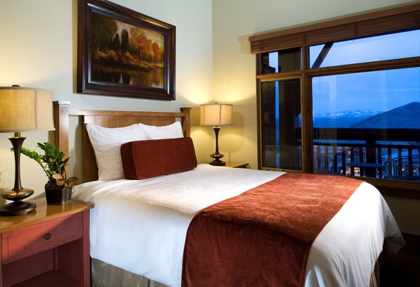 Ein Hotelzimmer mit einem großen Bett, zwei Nachttischlampen, einem Gemälde an der Wand und einem Fenster mit Blick auf Berge.