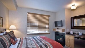 A hotel room with a bed, a television, a fireplace, and a kitchen area.