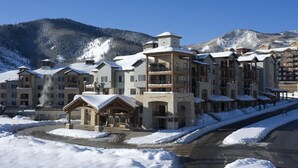 Un hôtel à plusieurs étages doté d’une cour intérieure, entouré de bâtiments recouverts de neige et avec des montagnes en toile de fond.