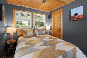 Une chambre à coucher avec un lit, deux fenêtres, une porte et un tableau accroché au mur.