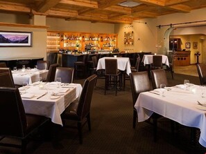 Un restaurante con mesas dispuestas para comer, una zona de bar con botellas y vistas a la montaña.