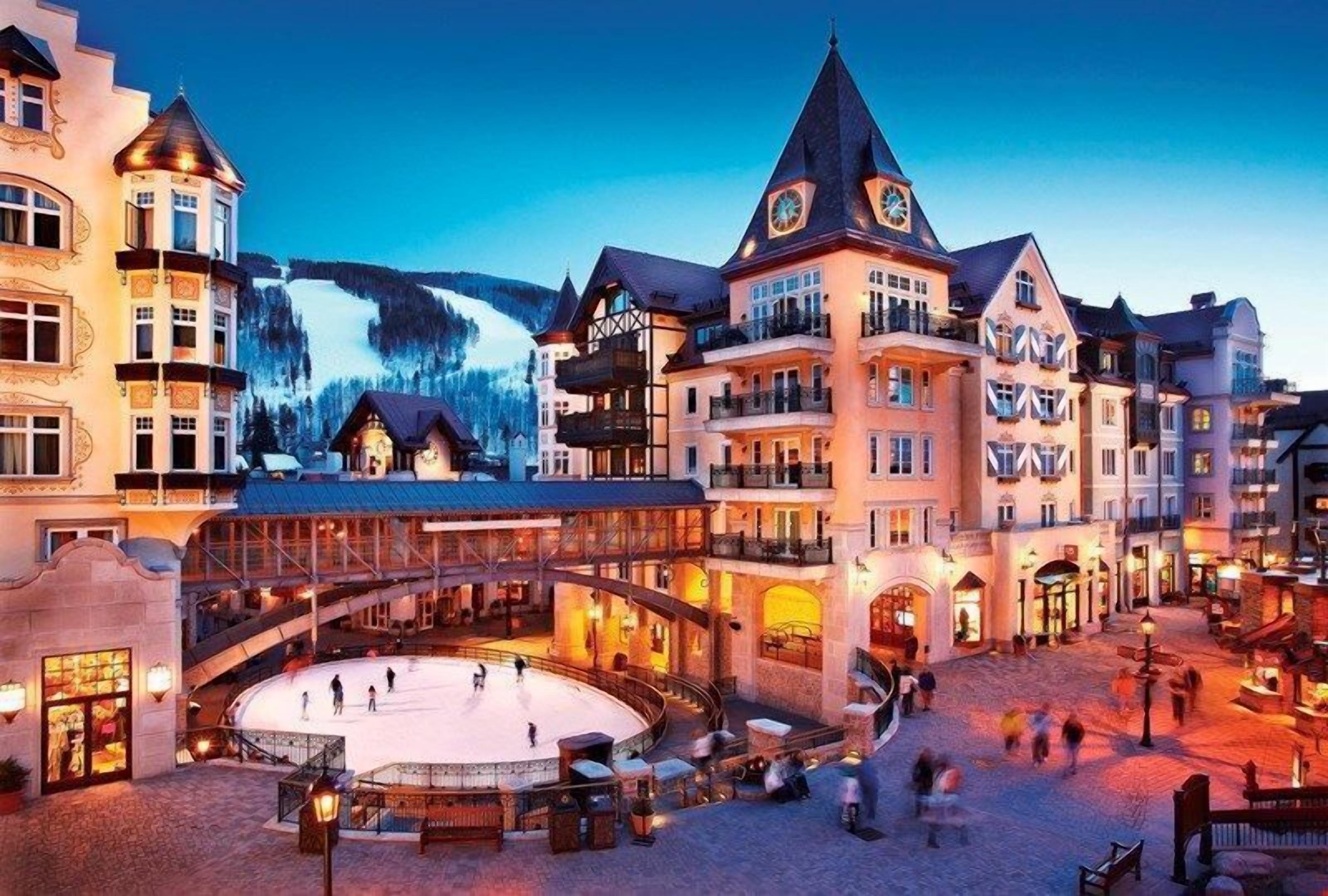 Ein historisches Gebäude mit einem zentralen Innenhof, einer Skipiste im Hintergrund und einer runden Eisbahn.