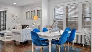 Una sala de estar moderna con comedor, que incluye una mesa blanca, sillas azules y una lámpara.