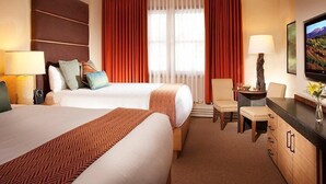 A hotel room with two beds, a desk, a chair, and a television.