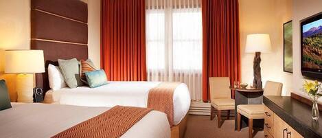 A hotel room with two beds, a desk, a chair, and a television.