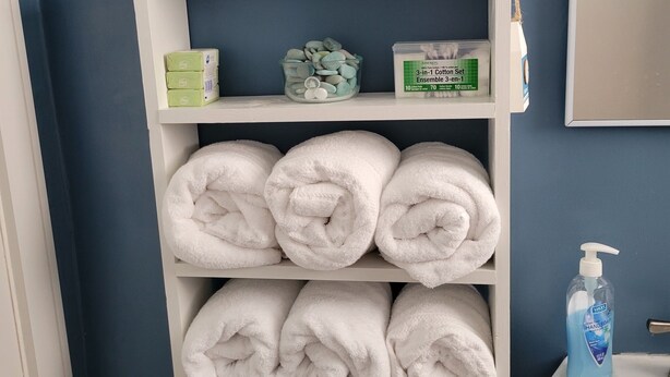 Une étagère dans la salle de bain avec des articles de toilette, un ensemble de produits en coton et des serviettes soigneusement pliées.