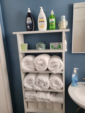 Une étagère dans la salle de bain avec des articles de toilette, un ensemble de produits en coton et des serviettes soigneusement pliées.