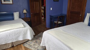 Une pièce avec deux lits, un bureau en bois, une chaise, une bibliothèque et une porte.