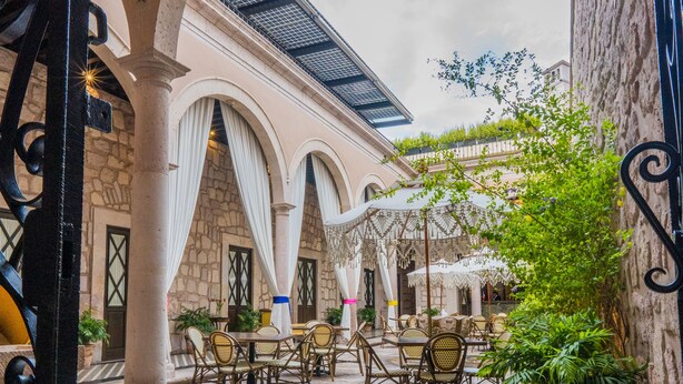 Un patio al aire libre con columnas de piedra, suelo de baldosas y mobiliario exterior.