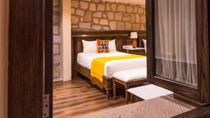 Un dormitorio con pared de piedra, cama con manta amarilla, mesita de noche con lámpara y ventana con cortinas.