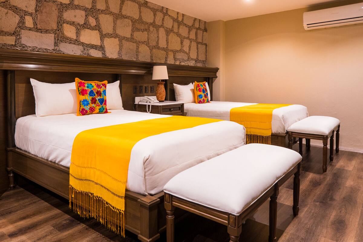 Een hotelkamer met een stenen muur, houten bedframes en een gele plaid.