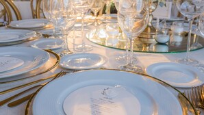 Una mesa dispuesta para un evento formal, con platos blancos, detalles dorados y copas de cristal.