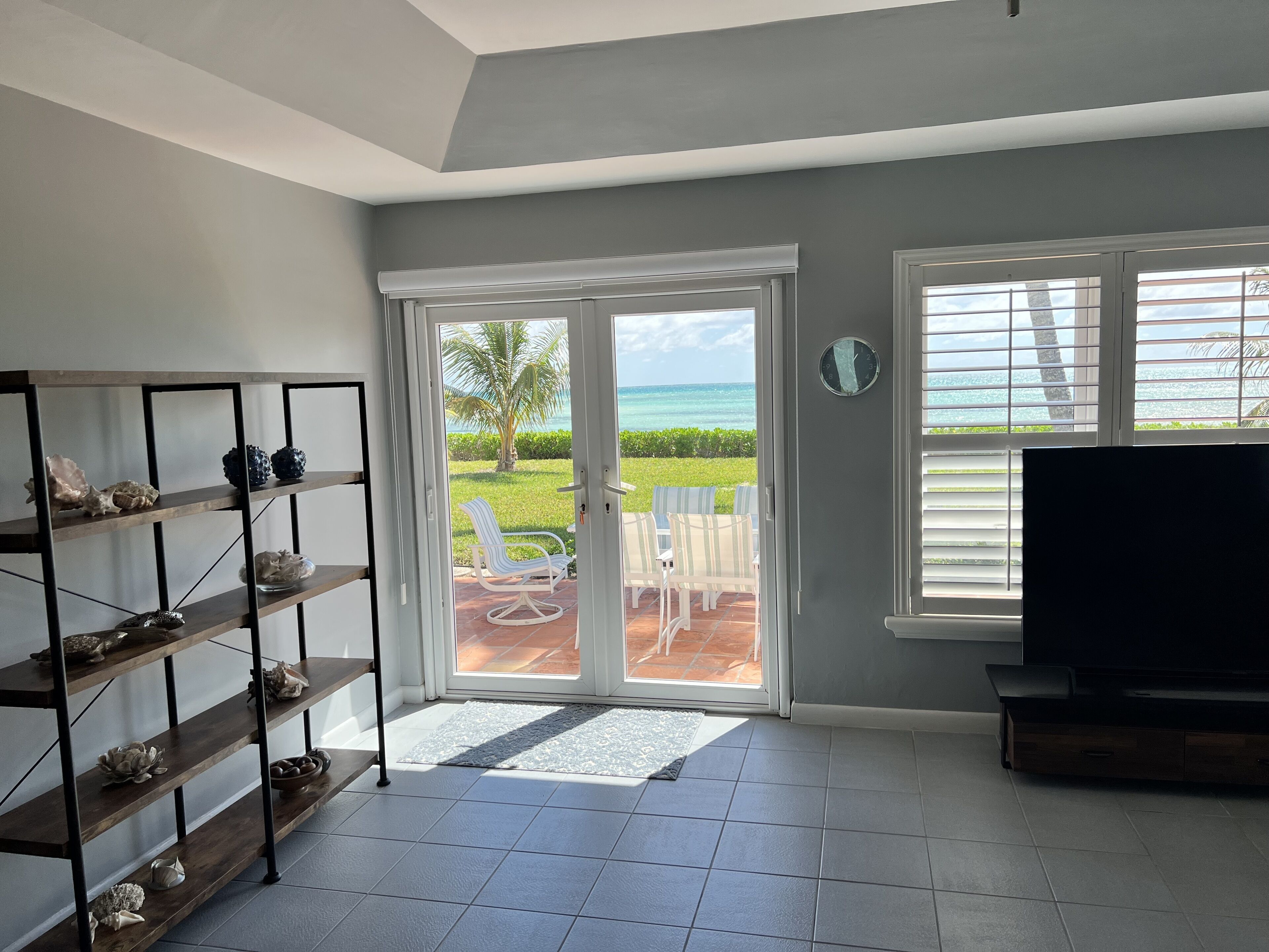 A living room with a view of the ocean, a TV, and a bookshelf.