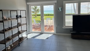 A living room with a view of the ocean, a TV, and a bookshelf.