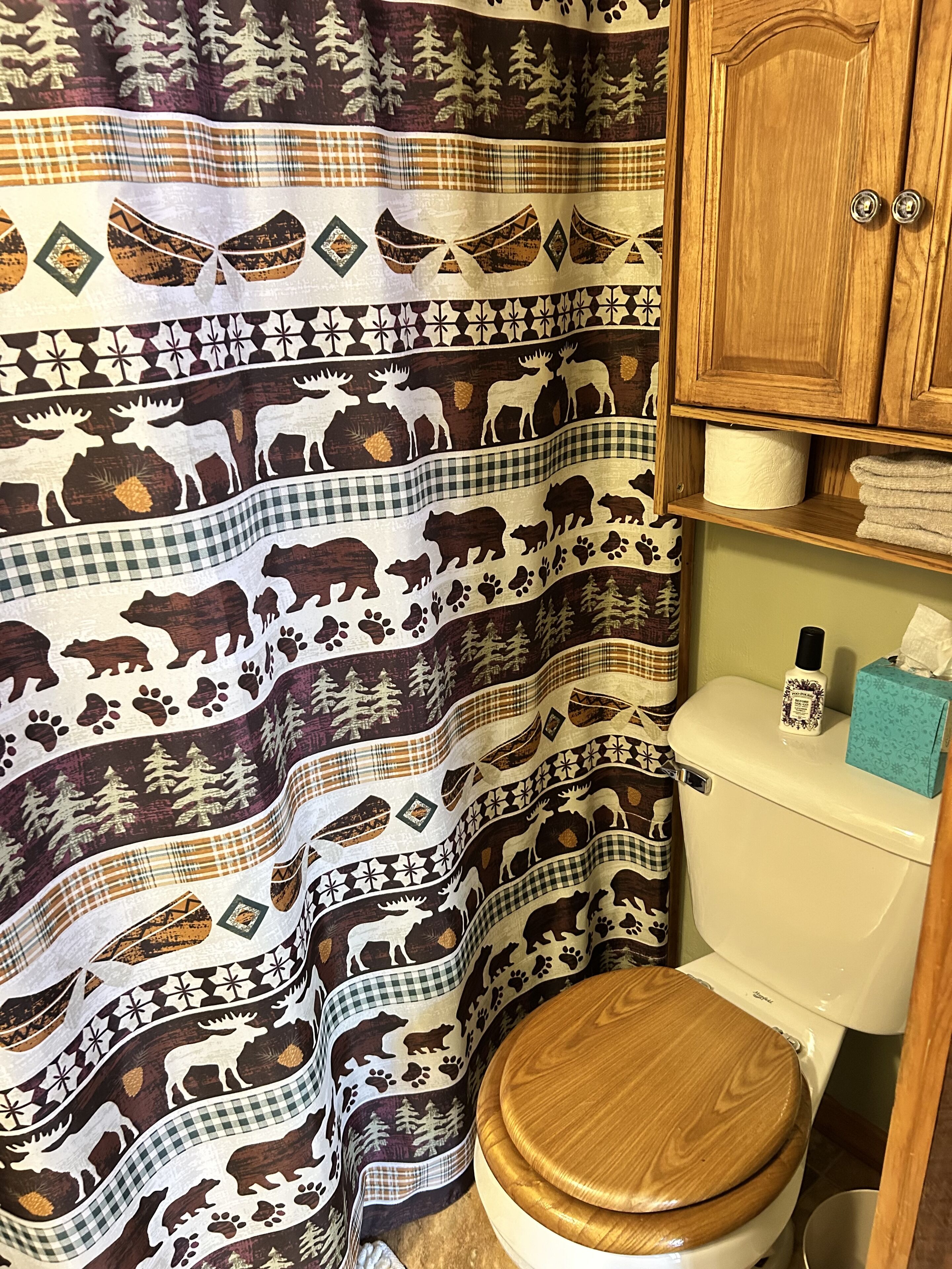A bathroom with a wooden toilet, a shower curtain with animal patterns, and a wooden cabinet with toiletries.