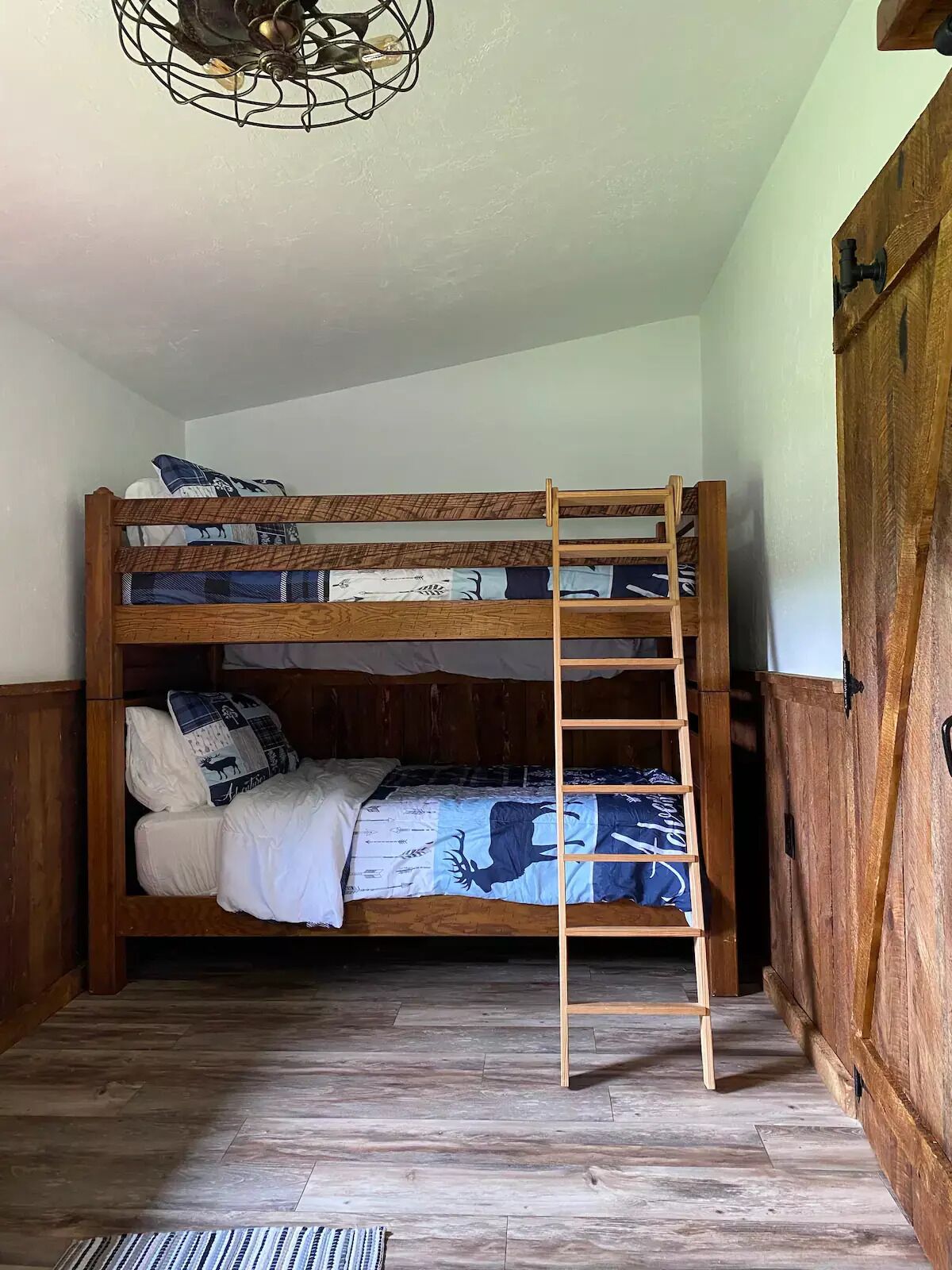 A bunk bed with a ladder, wooden walls, and a wooden floor.