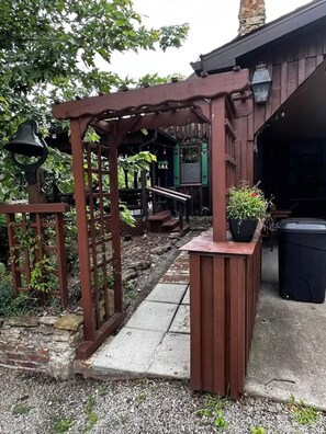 A wooden pergola with a bench, a planter, and a trash bin.
