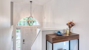 A hallway with a white door, a wooden console table with a vase of flowers, and a hanging light fixture. - Tranquil Urban Oasis in Bonney Lake (Bonney Lake)