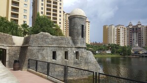 Una estructura de piedra con una cúpula y una torre cilíndrica, rodeada por una masa de agua y edificios modernos de gran altura al fondo.