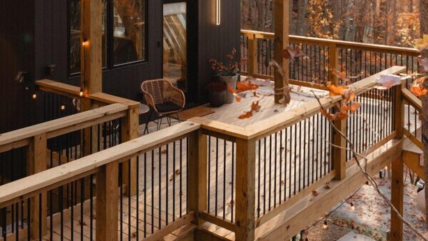 A cabin with a wooden deck, large windows, and a view of the surrounding forest. - Firefly Cabin at Out of Bounds Retreats (Banner Elk)