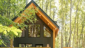 A two-story wooden cabin with a balcony, surrounded by trees. - Firefly Cabin at Out of Bounds Retreats (Banner Elk)
