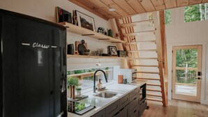 A modern kitchen with a black refrigerator, wooden shelves, and a large window. - Firefly Cabin at Out of Bounds Retreats (Banner Elk)