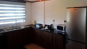 Eine kleine Küche mit Spüle, Mikrowelle, Kühlschrank und einem Fenster mit Jalousien.