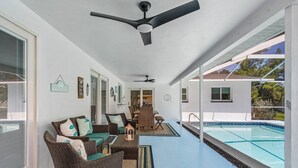 Eine überdachte Terrasse mit Korbmöbeln, einem Pool und Deckenventilatoren.