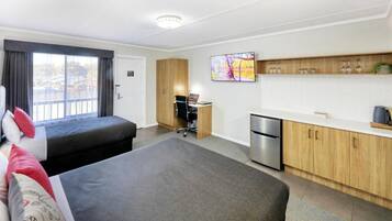 Een hotelkamer met een bed, een bureau met een computer, een koelkast en een keukenhoek met kastjes en een aanrecht.
