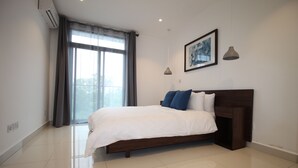 Un dormitori modern amb un llit gran, una finestra amb cortines, un quadre al mur i una làmpada penjant.