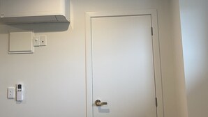 A white door with a handle, a white air conditioning unit mounted on the wall, and a light fixture on the ceiling. - Norton Motel (Hamilton)