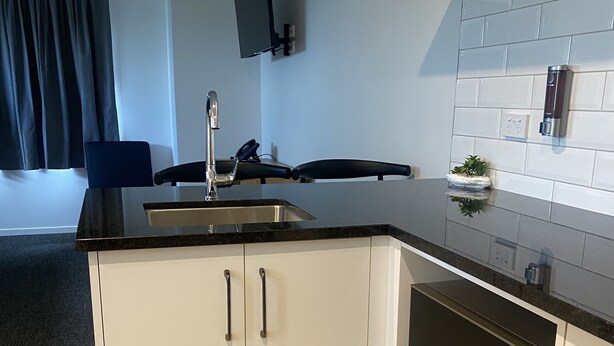 A modern kitchen with white cabinets, a black countertop, and a built-in microwave. - Norton Motel (Hamilton)